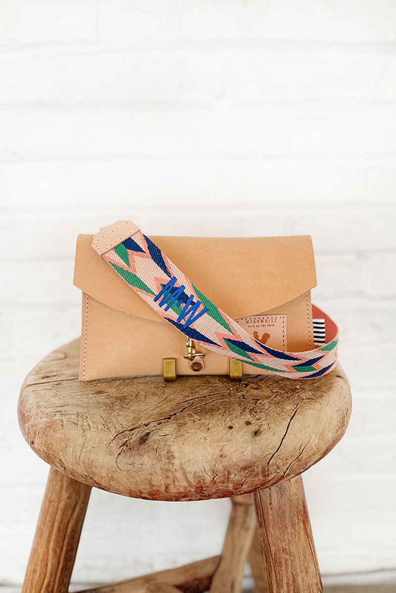 Light orange leather clutch on a stool with a multi-colored (orange/green) webbing crossbody strap