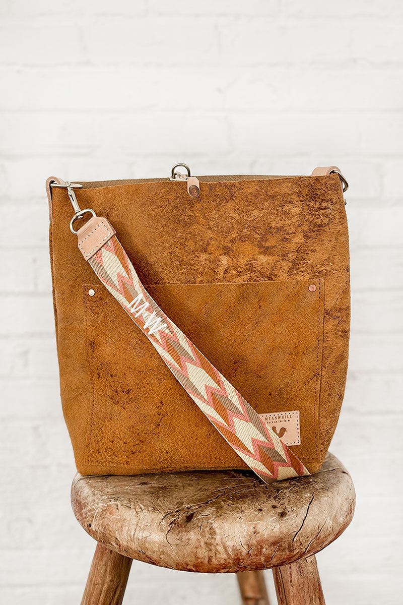 Brown leather bag on a stool with a orange and brown webbing crossbody strap