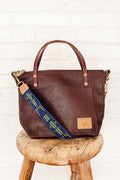 Brown leather bag on a stool with a blue and yellow webbing crossbody strap