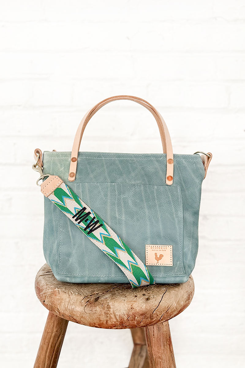 Blue leather bag with tan straps on a stool with a green webbing strap