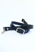 A black leather purse strap with a gold buckle wrapped in a coil