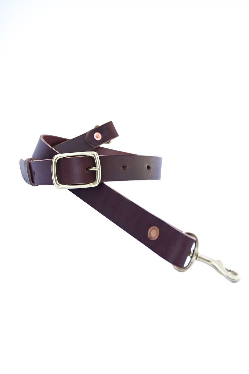 A dark brown leather purse strap with a gold buckle wrapped in a coil