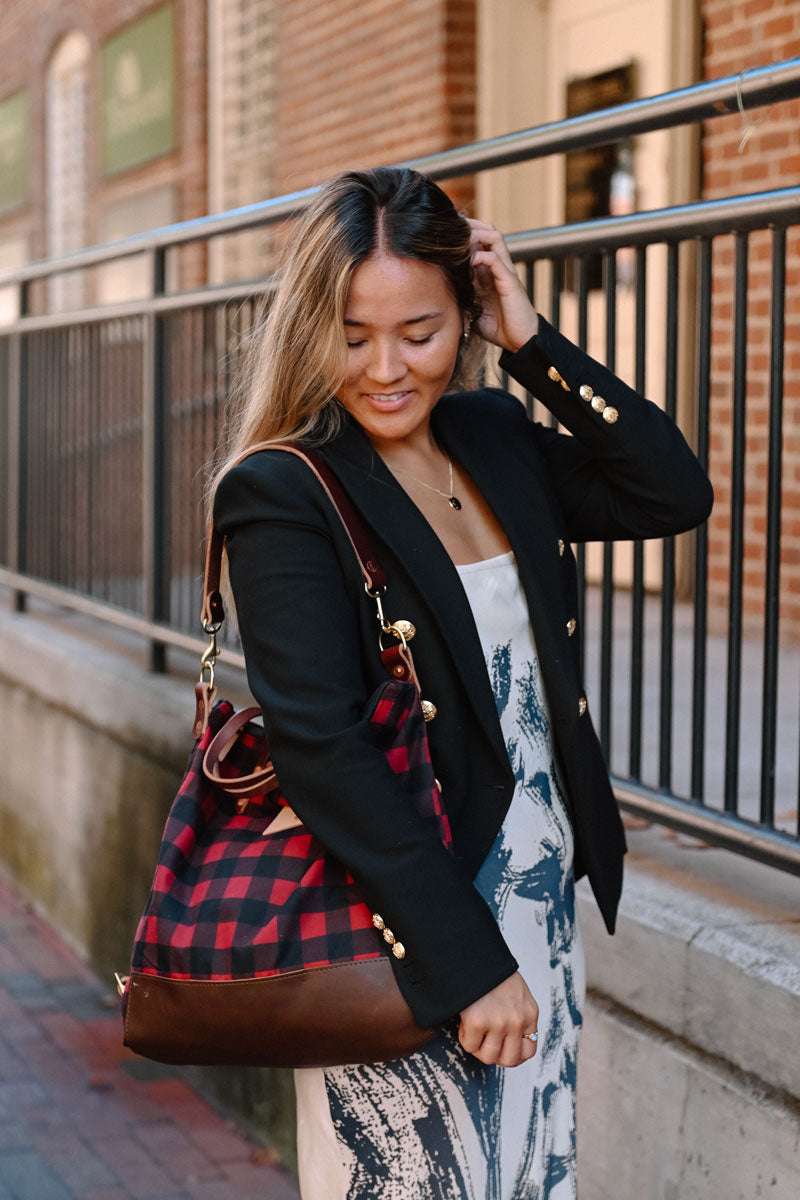 Woman tucking her hair behind her ear and wearing a red/black plaid leather convertible backpack on her shoulder