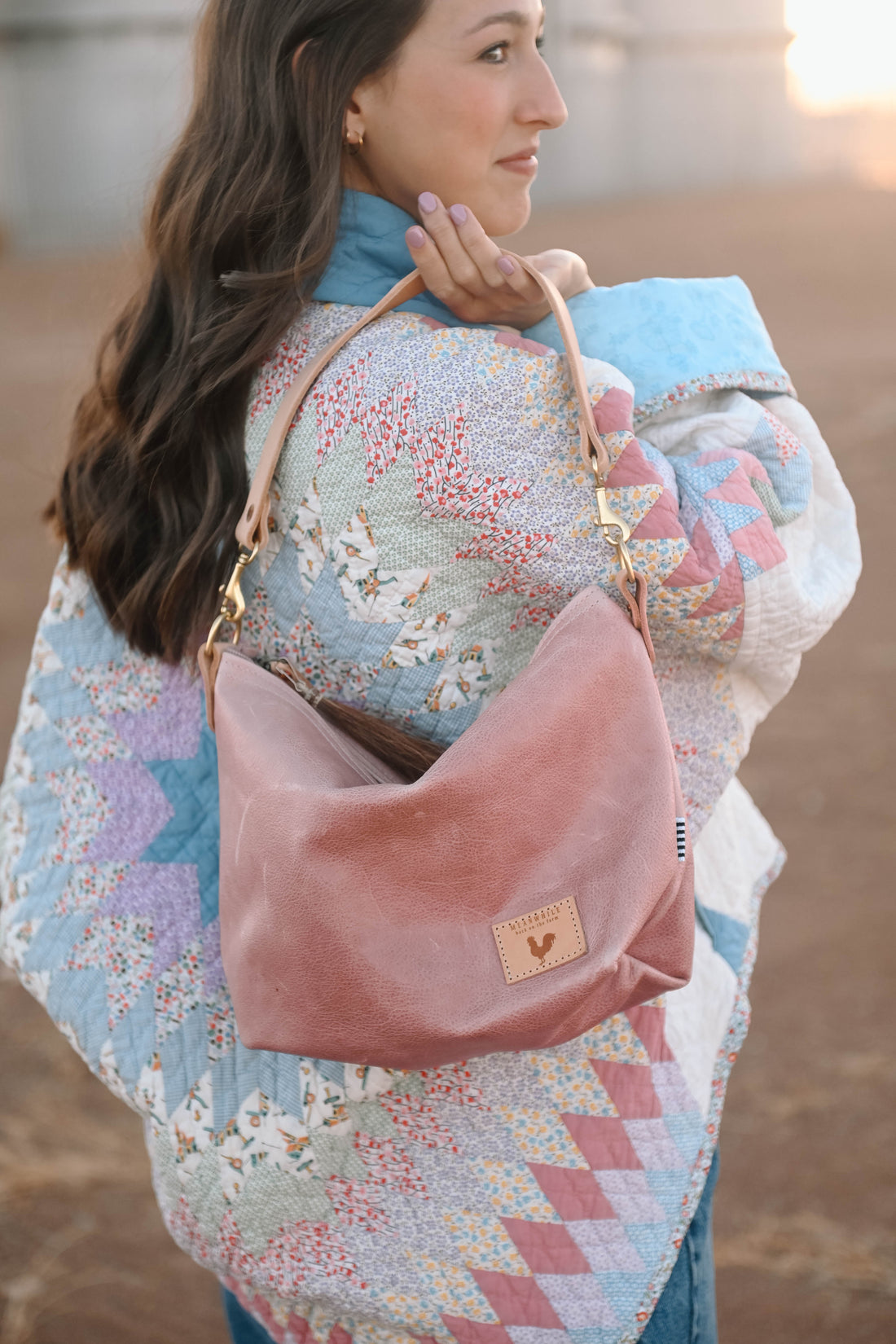 A woman wearing over the shoulder the rose pink bag with the meanwhile logo and a brown tassel zipper.