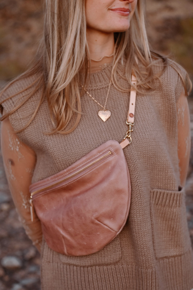 Model wearing zippered rose colored cross body bag.