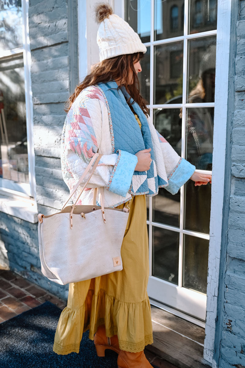 Model entering and building and carrying a birch white leather tote bag with cream colored straps.