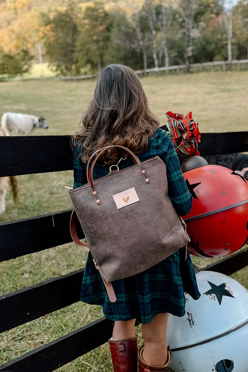 Woman looking over farm fence while wearing a large brown mottled bag with brown leather straps.