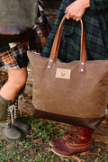 Woman holding a brown leather handbag with dark brown leather bottom and brown leather straps.