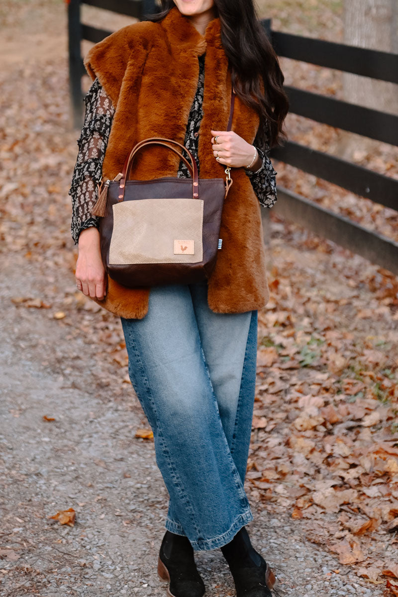 Model reaching into handbag. Handbag is dark leather with a cream colored brushed leather front pocket