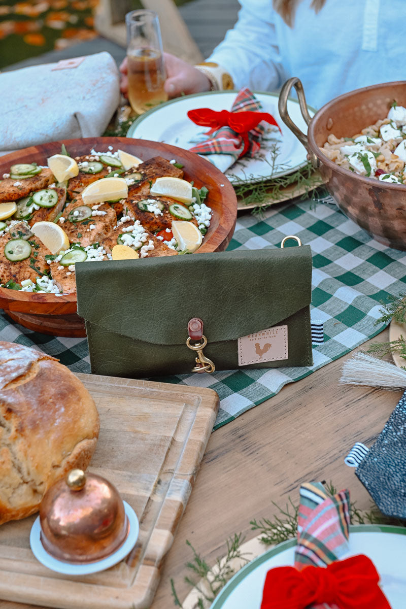 Picture of a beautifully decorated holiday season table with various foods. A green leather clutch is propped up in the middle of the table.