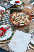 A festively decorated table with fresh baked bread. An off white zippered clutch sits next to the Christmas dishes. 