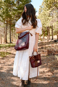 Woman in the forest in a white dress wearing a red leather tote bag and holding a red leather small tote