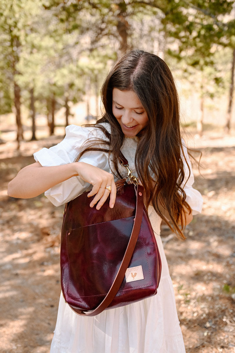 Woman in the forest reaching inside a red leather tote bag