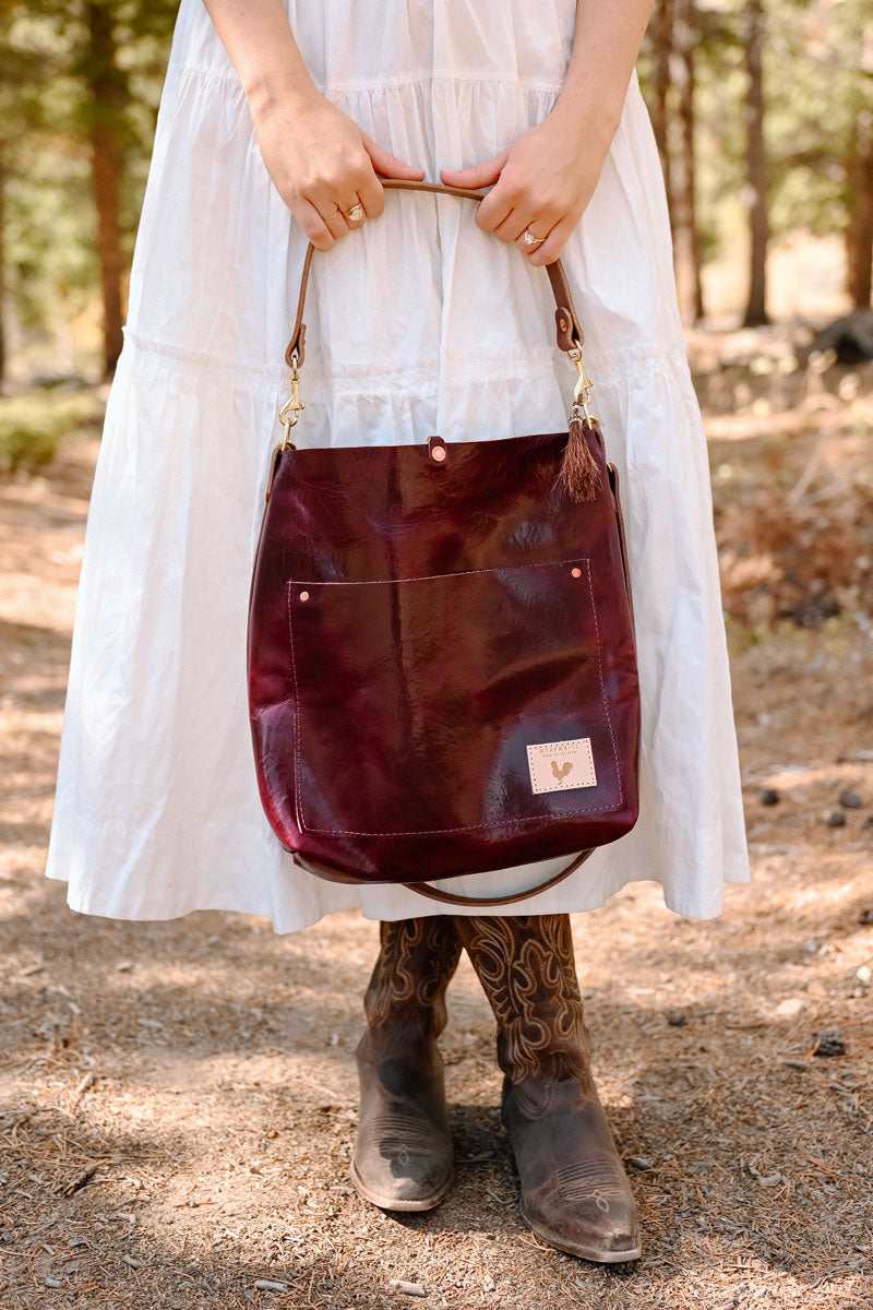 Woman in the forest reaching inside a red leather tote bag