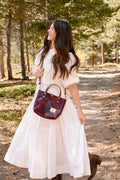 Woman in the forest in a white dress wearing a red leather small tote