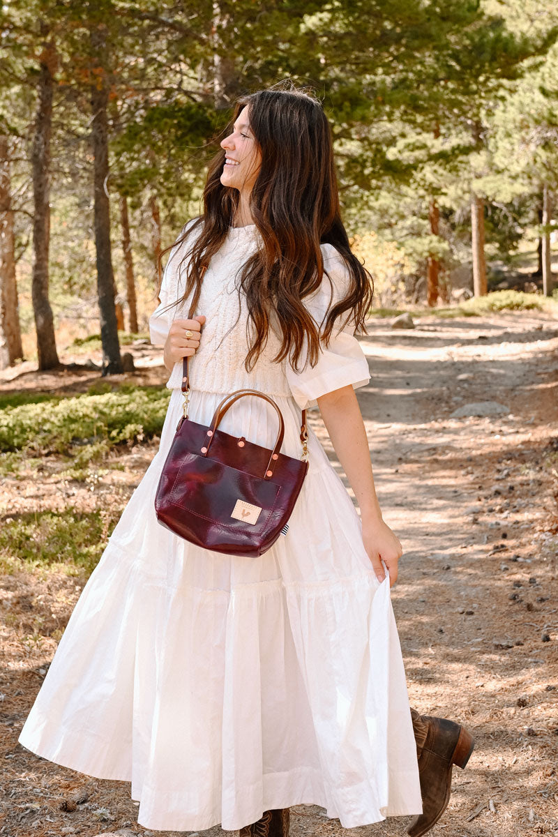 Woman in the forest in a white dress wearing a red leather small tote