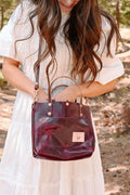 Woman in the forest in a white dress wearing a red leather small tote and reaching into it