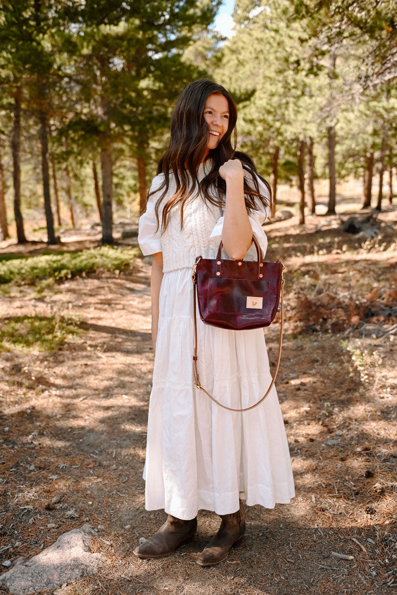 Woman in the forest in a white dress holding a red leather small tote