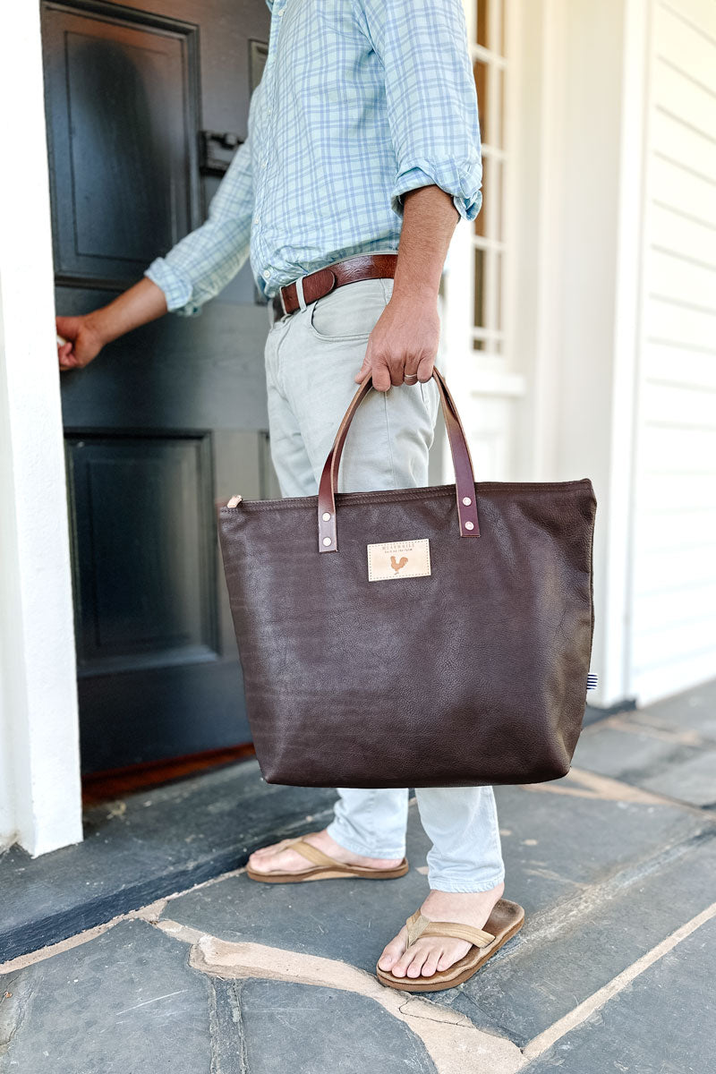 Man putting a small brown handbag into a large brown leather tote bag