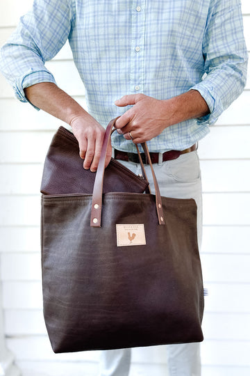 Man putting a small brown handbag into a large brown leather tote bag