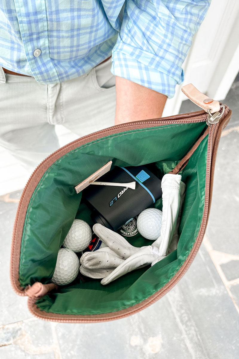 Green lining of a small brown leather hand bag with miscellaneous items (golf balls, glove, pick)