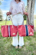 Girl holding two bags: orange leather large tote bag with a red/white stripe in the middle and a matching one with a green/white stripe in the middle 