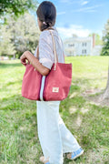 Girl wearing an orange leather large tote bag with a red/white stripe in the middle on her shoulder