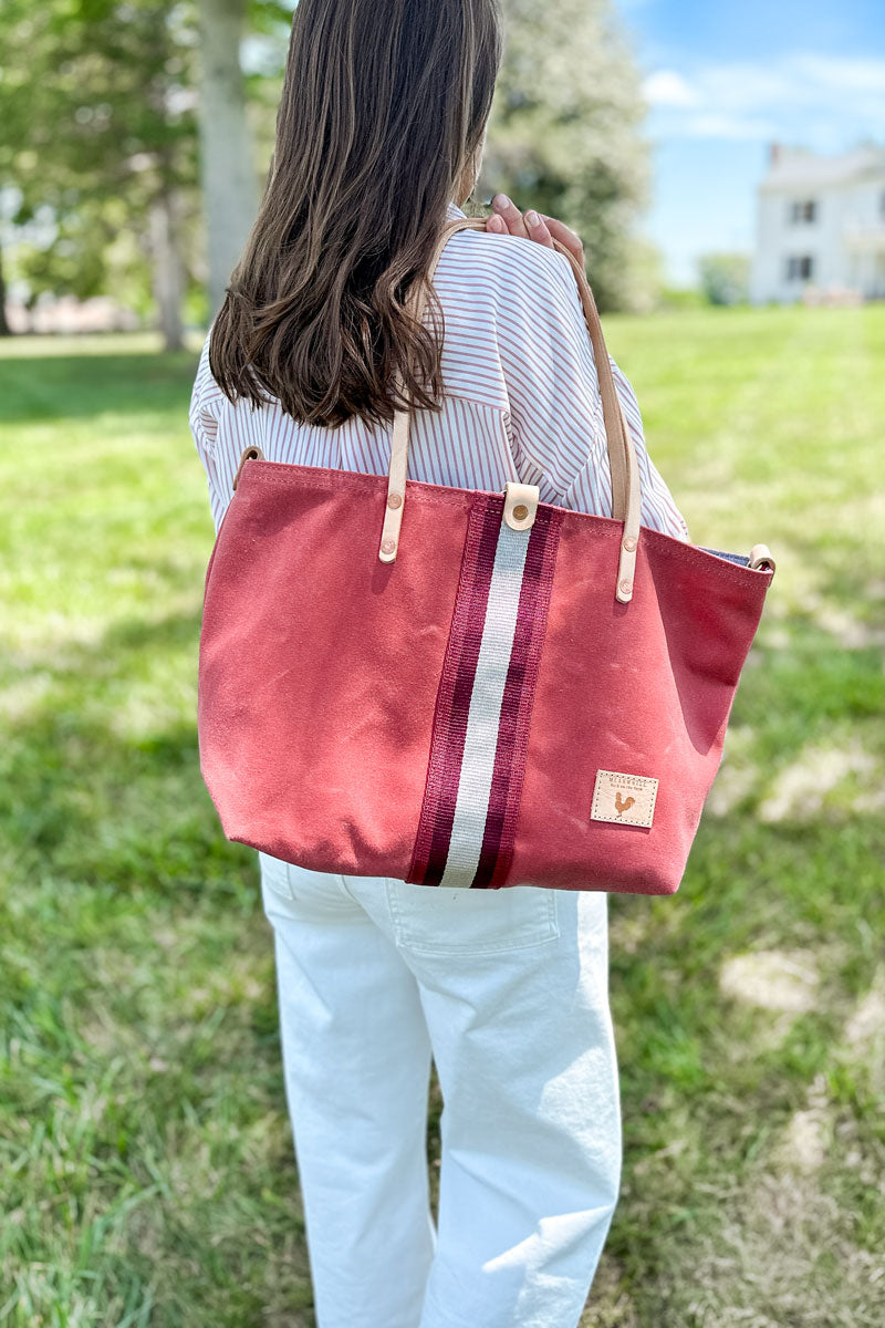 Girl wearing an orange leather large tote bag with a red/white stripe in the middle on her shoulder