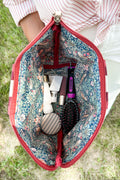 Girl showing inside floral blue lining of the small orange/red striped leather pouch with different accessories inside