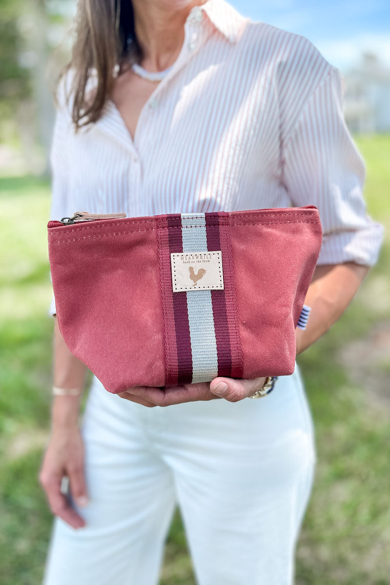 Girl holding a small orange leather clutch/pouch bag with a red/white stripe in the middle