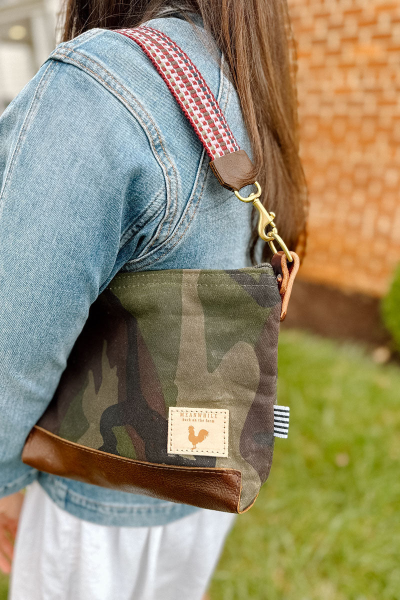 Woman wearing a brown/camo leather purse with a red/pink webbing crossbody strap on her shoulder