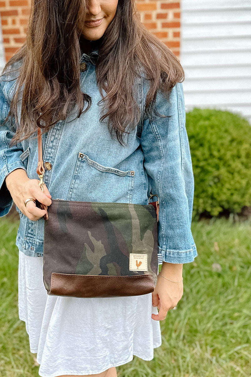 Woman wearing a brown/camo leather purse with a red/pink webbing crossbody strap on her shoulder