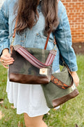 Woman wearing a green/brown leather purse on her shoulder with a brown/orange webbing crossbody strap and a brown/camo leather purse