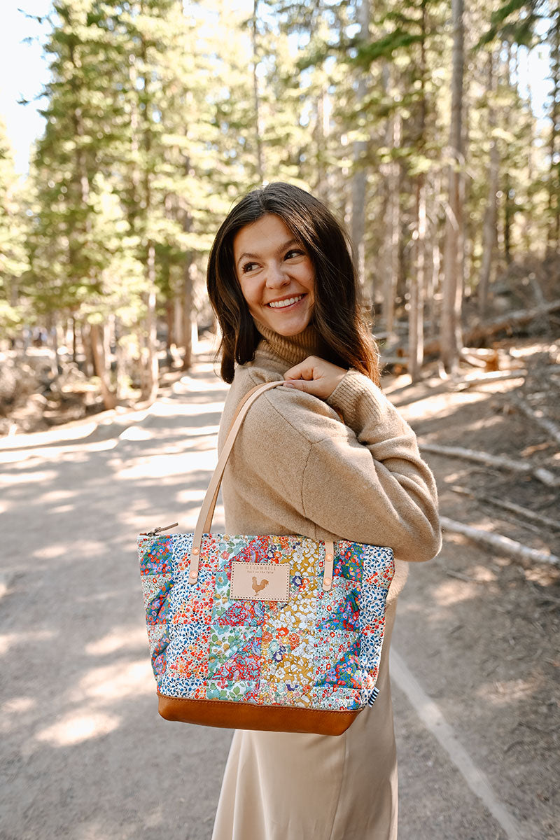 Model holding floral quilted bag with tan handles and leather bottom