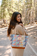 Model displaying quilted floral bag with cream colored handle and tan leather bottom.