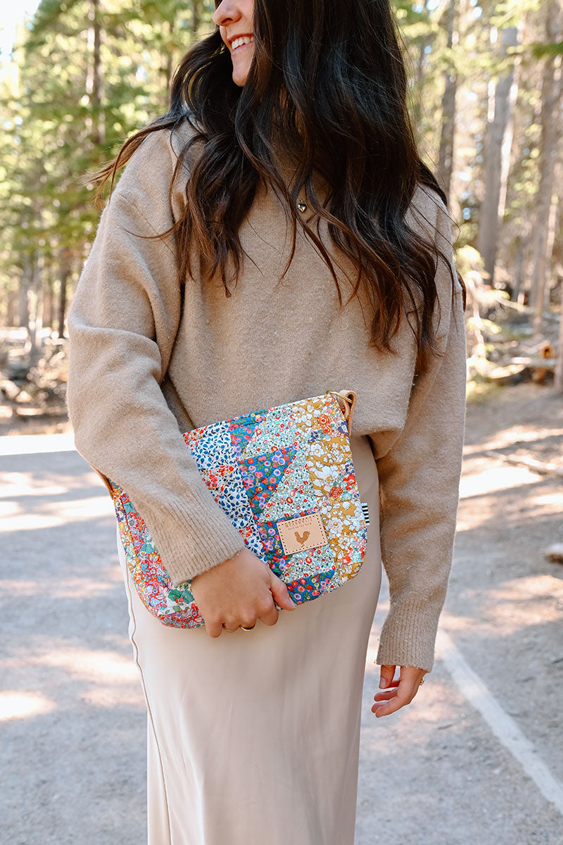 Model holding medium sized quilted floral handbag with no handles or straps