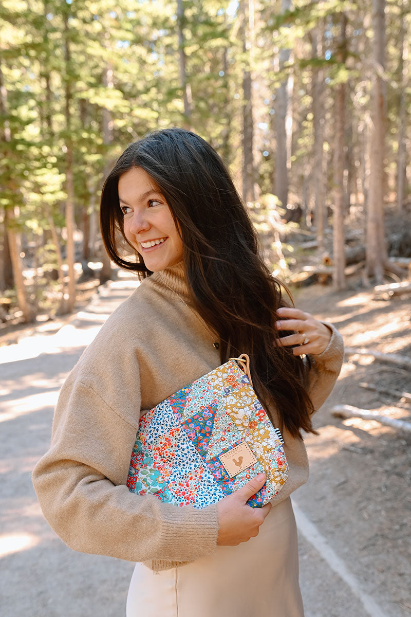 Model looking back over her shoulder holding a floral quilted hand bag with no straps