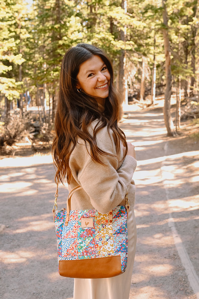 Model smiling at camera wearing a quilted floral print bag with cream colored straps and tan leather bottom