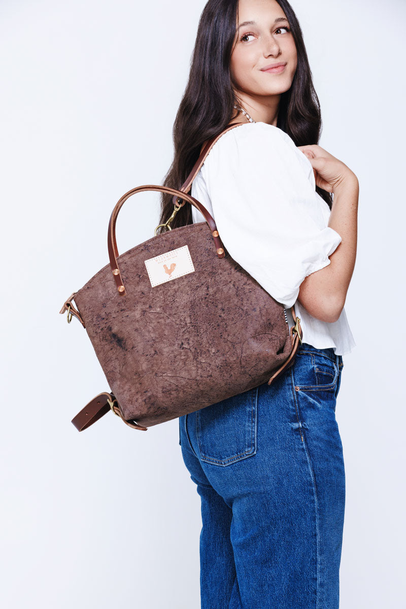 Model wearing brown leather backpack style bag with brown arm strap