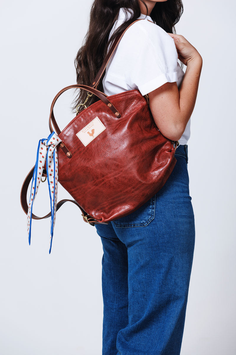 Model wearing red leather back pack style tote with blue and white ribbon tied to it.