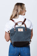 Model wearing slate colored back pack style bag with brown straps.