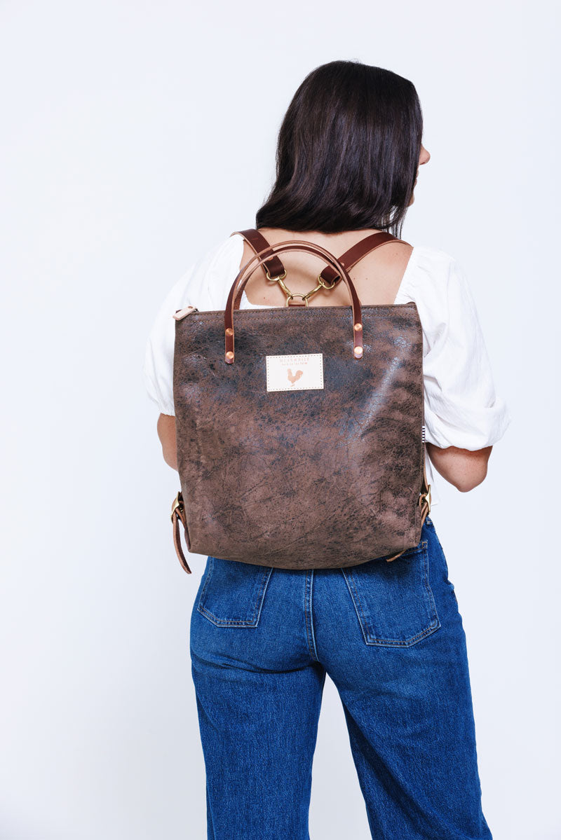 Model wearing brown leather back pack style bag with brown straps.