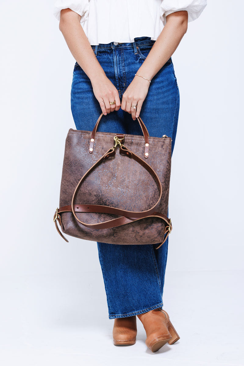 Model wearing brown leather back pack style bag with brown straps