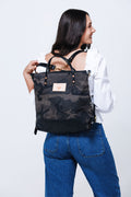 Model putting on dark camouflage backpack style bag with arm straps.