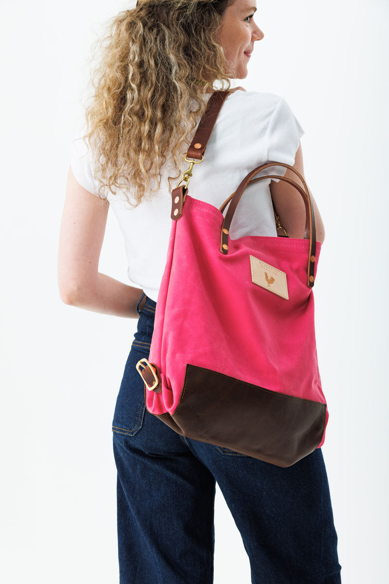 A woman wearing the bright pink backpack with dark brown straps and the meanwhile logo.