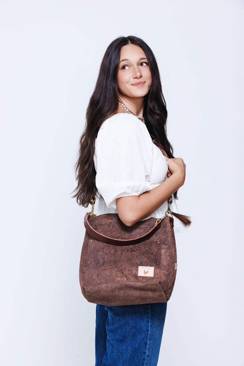 Model wearing a large brown leather shoulder bag with brown arm strap and tassle