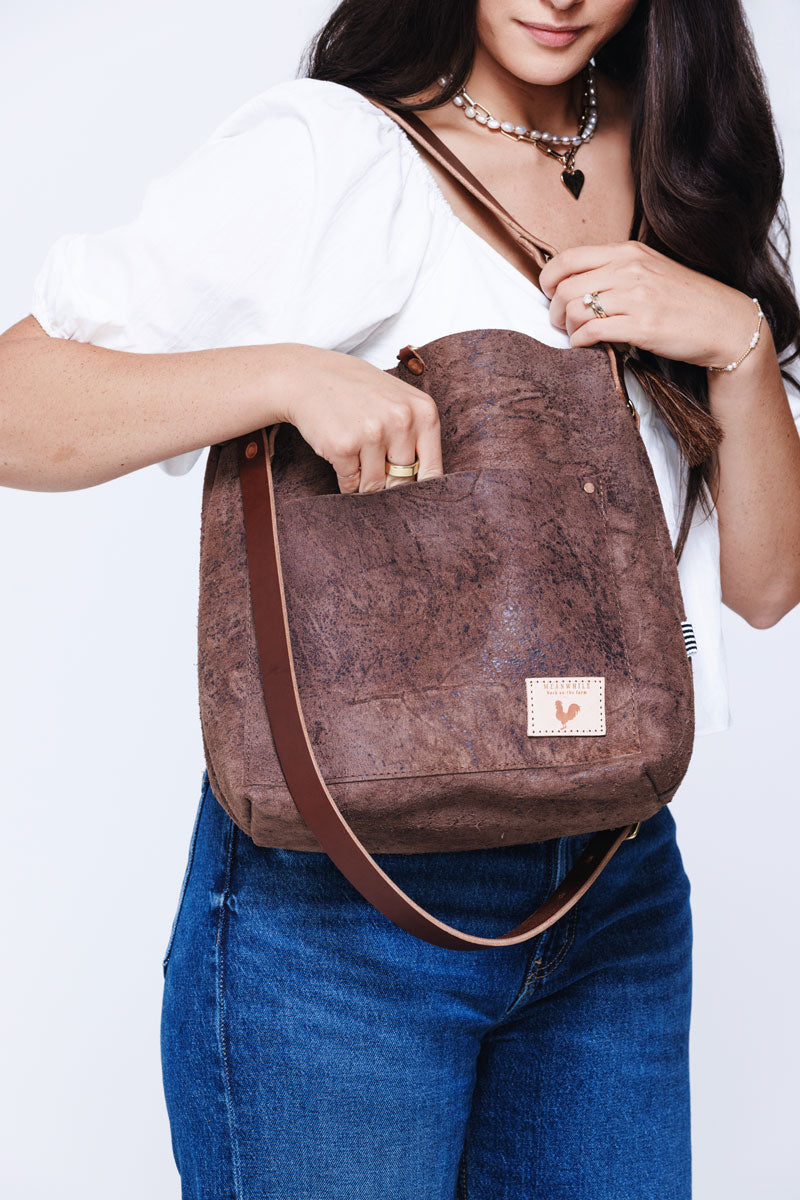 Model wearing a large brown leather shoulder bag with brown arm strap and tassle