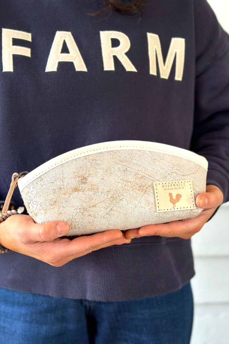 Model wearing a dark blue sweatshirt with Farm written on front holding a small off white zippered pouch