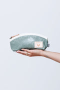 Model's hand holding a green white zippered pouch or make up case.