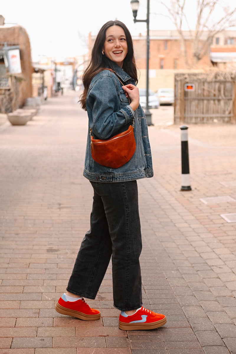 Model wearing a reddish tan leather fanny pack bag as a cross body bag.